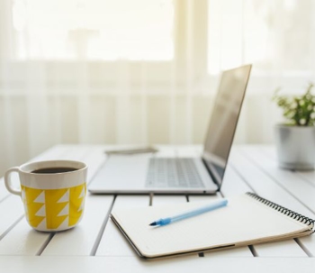 Laptop, notepad, and a coffee mug on top of a white desk.